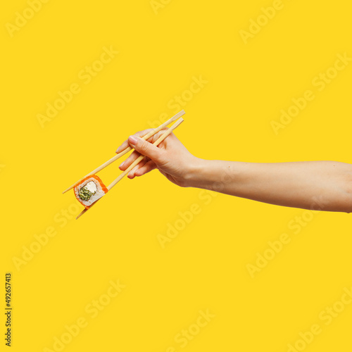 Woman's hand holds sticks sushi roll yellow background