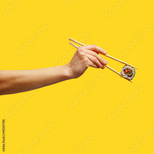 Woman's hand holds sticks sushi roll yellow background