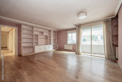 Large empty living room with a terrace  parquet floors and plaster and wood shelving on a wall painted pink