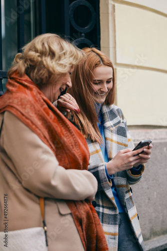 A grandmother and her grandchild standing on the street and reading messages on the phone.