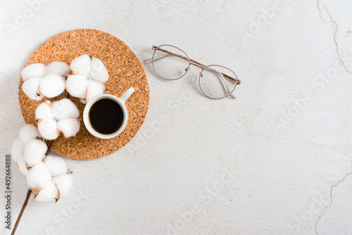 A cup of coffee, a branch of cotton and glasses on a light background. Workplace organization. Eco lifestyle