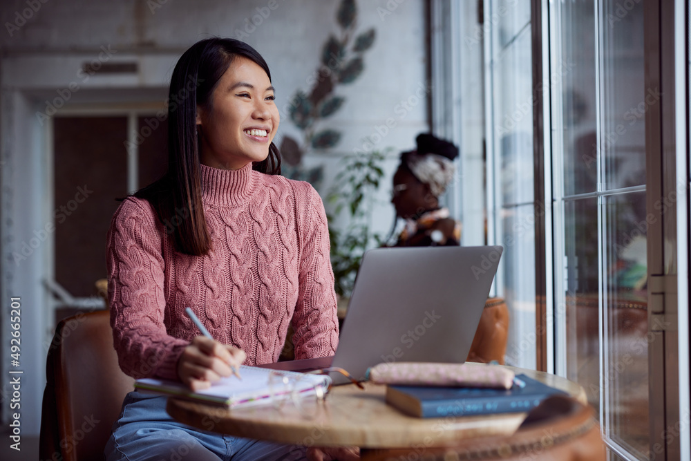 A happy Asian girl follows online lectures on the laptop at a cafe. A happy Asian girl follows online lectures on the laptop at a cafe.