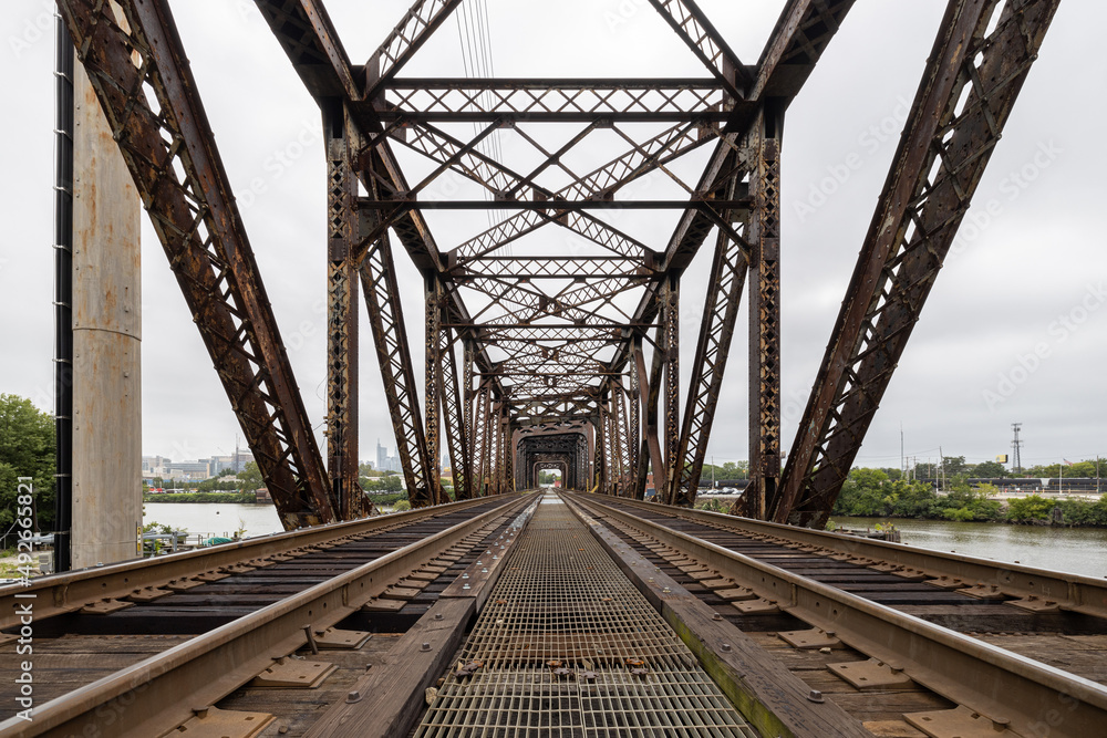 Two railroad train tracks lead into a rusty metal trestle bridge crossing the Schuylkill River in Philadelphia, Pennsylvania, USA