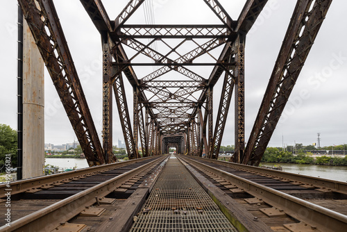 Fototapeta Naklejka Na Ścianę i Meble -  Two railroad train tracks lead into a rusty metal trestle bridge crossing the Schuylkill River in Philadelphia, Pennsylvania, USA