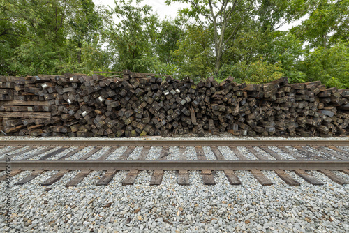 Brown railroad ties piled up next to active train tracks photo