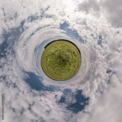 green tiny planet in blue sky with beautiful clouds. Transformation of spherical panorama 360 degrees. Spherical abstract aerial view. Curvature of space.