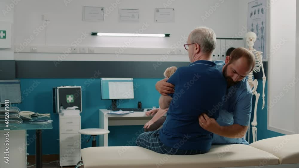 Male specialist helping old patient to crack back bones at physical therapy appointment. Osteopath using stretching procedure to increase mobility and give support for injury recovery. Male specialist helping old patient to crack back bones at physical therapy appointment. Osteopath using stretching procedure to increase mobility and give support for injury recovery.
