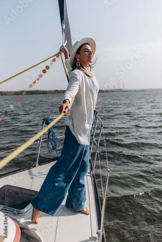 beautiful young woman in a hat stands on a yacht