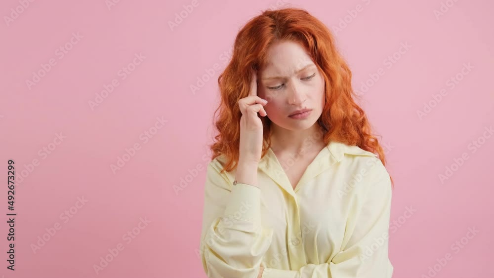 Seriously thinking red hair young girl tries to concentrate on something holding her fingers to the temple standing on pink background. Seriously thinking red hair young girl tries to concentrate on something holding her fingers to the temple standing on pink background.