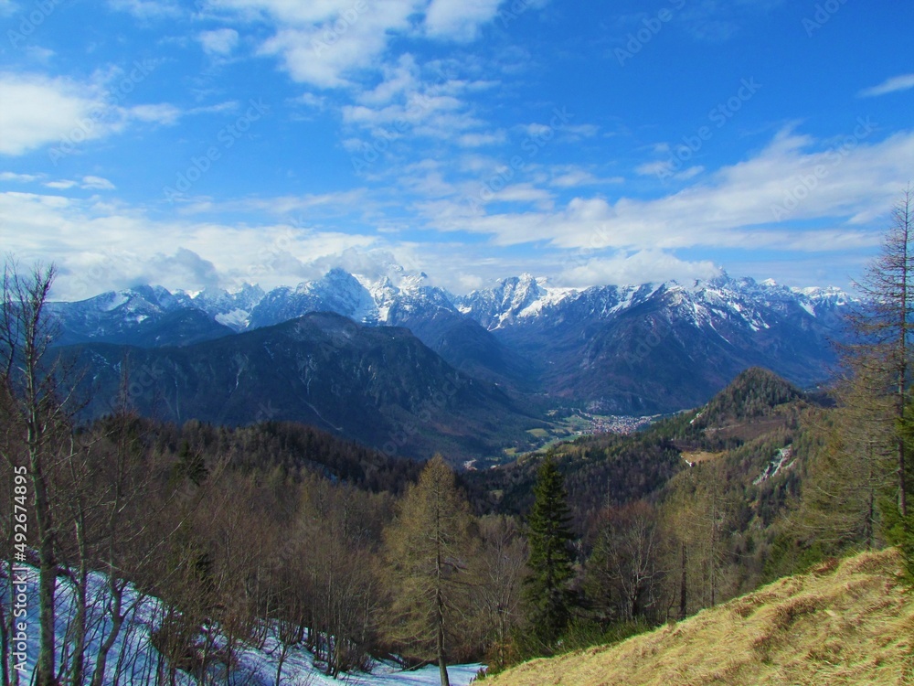 View of mountains above glacial valleys of Vrata in Triglav national park and Julian alps covered in snow and shrouded in clouds incl Triglav and Skrlatica and the village of Mojstrana in Slovenia