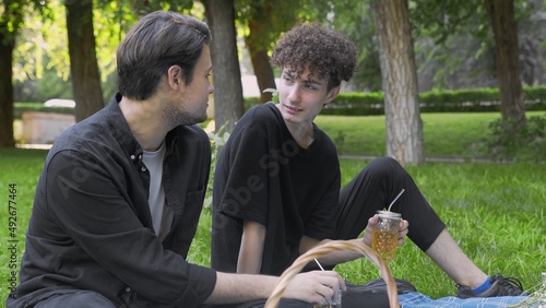 Two young guys are talking at a picnic in the park in the summer. LGBT
