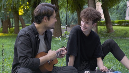 A guy plays the ukulele to another guy in nature in the summer. LGBT
