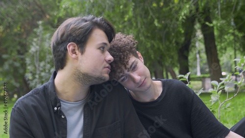 The guy slowly lowers his head on the shoulder of another guy in nature in the summer. LGBT