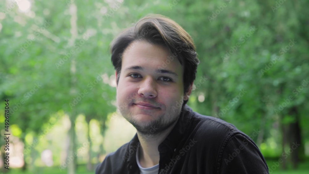 A young guy smiles and laughs, looking at the camera in nature in the summer A young guy smiles and laughs, looking at the camera in nature in the summer