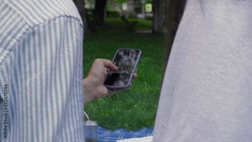 A man's hand holds a phone and flips through photos in nature in the summer