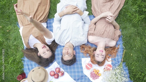 A guy and two girls in the summer lie on a blanket in nature and communicate top view