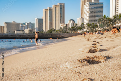 Footprints in the sand at Waikiki Beach in Honolulu, Hawaii, with the city skyline beyond. © Page Light Studios