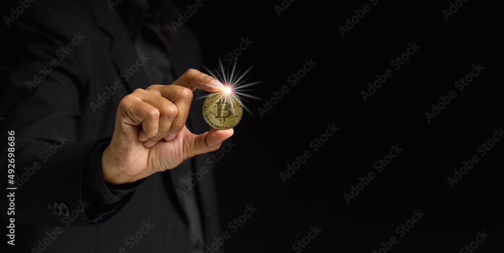 Fototapeta premium Businessman holding a bitcoin coin while standing over a black background