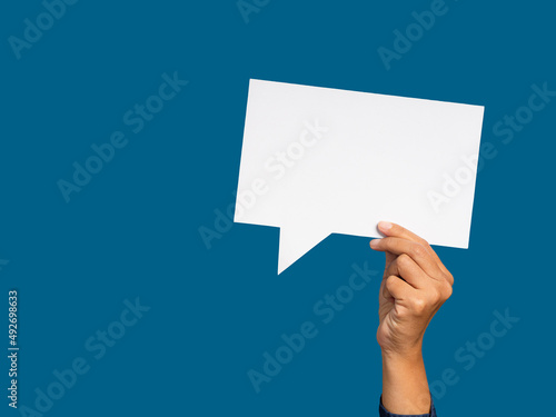 A speech bubble concept. Hand holding of an empty white speech bubble against a blue background