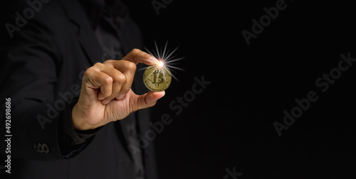 Businessman holding a bitcoin coin while standing over a black background