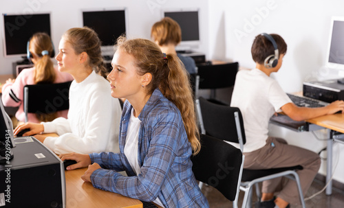 Portrait of a fifteen-year-old schoolgirl studying at a computer in a class at an informatics lesson with classmates