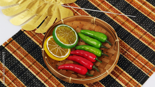 artificial green chili red chili lime yellow leaf in the basket on traditional mat studio photo