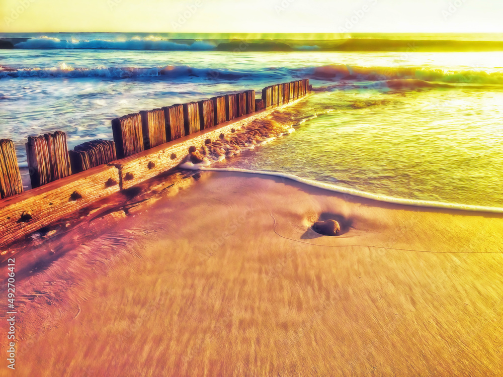 Sunshine over incoming surf and wooden fence on beach