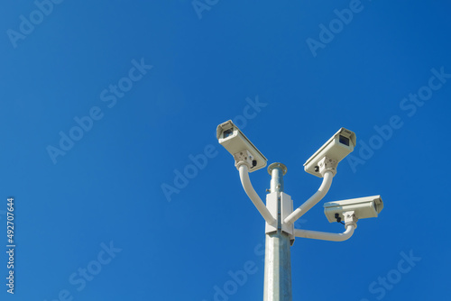 Three CCTV surveillance cameras mounted on a pole against blue sky