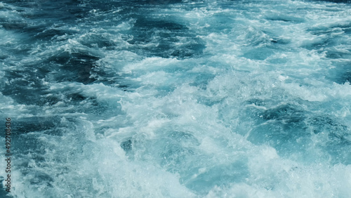 Close-up, beautiful splashes of water from motor yacht. Boiling clear turquoise water on high seas. Water rises in waves sprays into small crystal droplets creating white foam