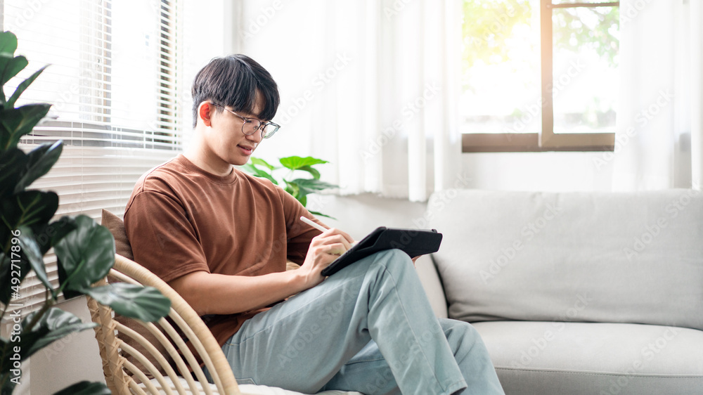 Technology Concept The male with his casual T-shirt and jeans sitting comfortably on the wooden chair and doing touchscreen for checking the web browser on the iPad. Technology Concept The male with his casual T-shirt and jeans sitting comfortably on the wooden chair and doing touchscreen for checking the web browser on the iPad.