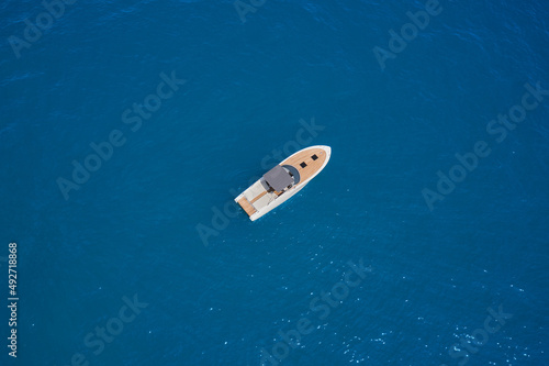 Modern boat with wooden trim top view. Boat with a gray awning in the parking lot aerial view. One boat on blue water drone view.