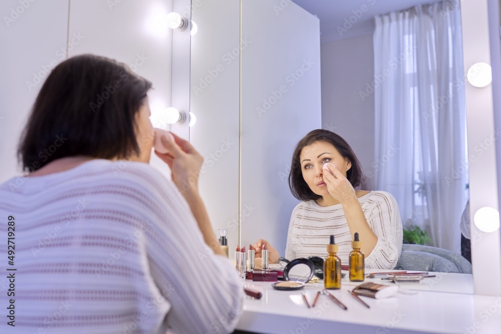 Beautiful middle aged woman doing makeup in front of a mirror. Beautiful middle aged woman doing makeup in front of a mirror.