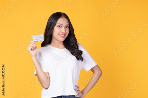 Portrait of a happy young asian woman wearing white shirt holding bank card  credit card isolated on yellow background. Business online shopping concept.