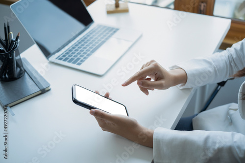 Cropped image of businesswoman sitting in front of laptop computer at office desk and using mobile phone.