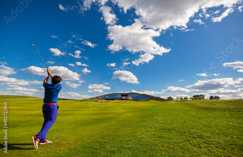 Man golf player teeing off the ball, view from behind. Space for text. Sport playground for golf concept - wide landscape as background for your lettering about golf playing. Royal sport.