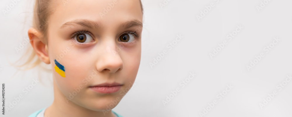 face of a frightened girl, a painted heart on the cheek in yellow-blue colors of the Ukrainian flag. face of a frightened girl, a painted heart on the cheek in yellow-blue colors of the Ukrainian flag.