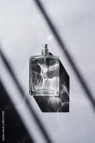 Transparent bottle of perfume with spray on a grey background. Beautiful natural light and shadows. Mockup of clear glass fragrance without lid . Cosmetics packaging container top view.