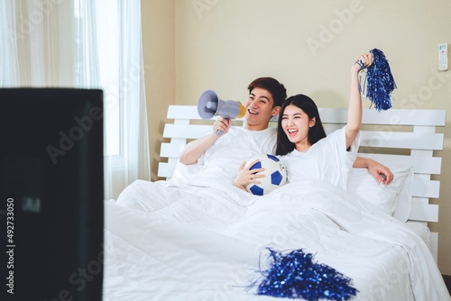 Teenage couple lying at home watching television tv sport football soccer game celebrating win goal.