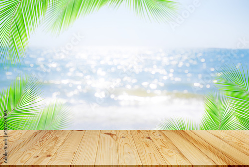Table on sea with palm leaves background.empty desk wooden on blur blue ocean sand with bright whithe bokeh at coast. mockup counter bar montage on blurry water.tourism travel tropical summer holiday.