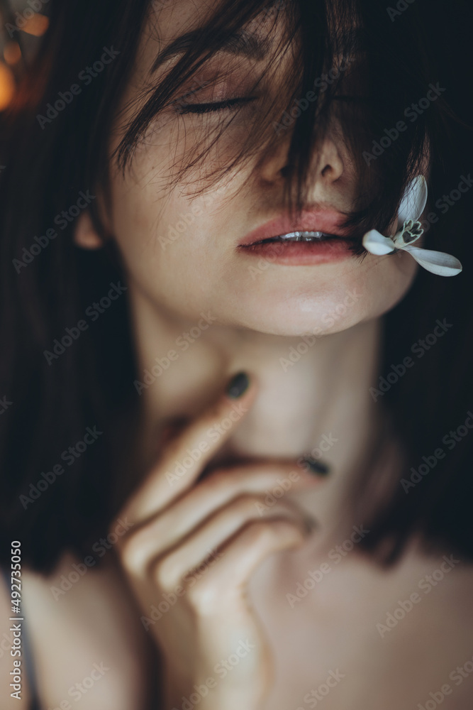 Obraz premium Portrait of a woman with a flower. A beautiful girl holds a snowdrop flower near her face. High quality photo