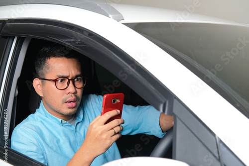 Adult Asian man looking to his mobile phone with serious expression while driving a car photo