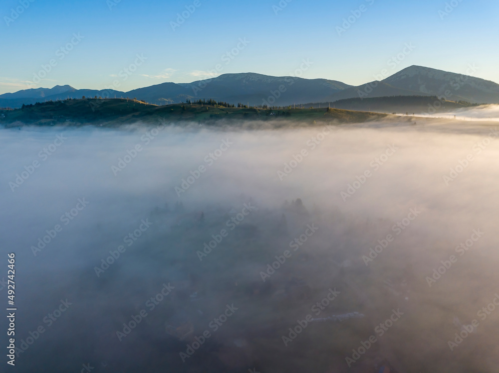 Sunny morning in the foggy Carpathians. A thick layer of fog covers the mountains. Aerial drone view.