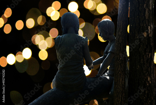 silhouette couple of young person statue sitting together on large tree brunches in the night with bokeh light background,
