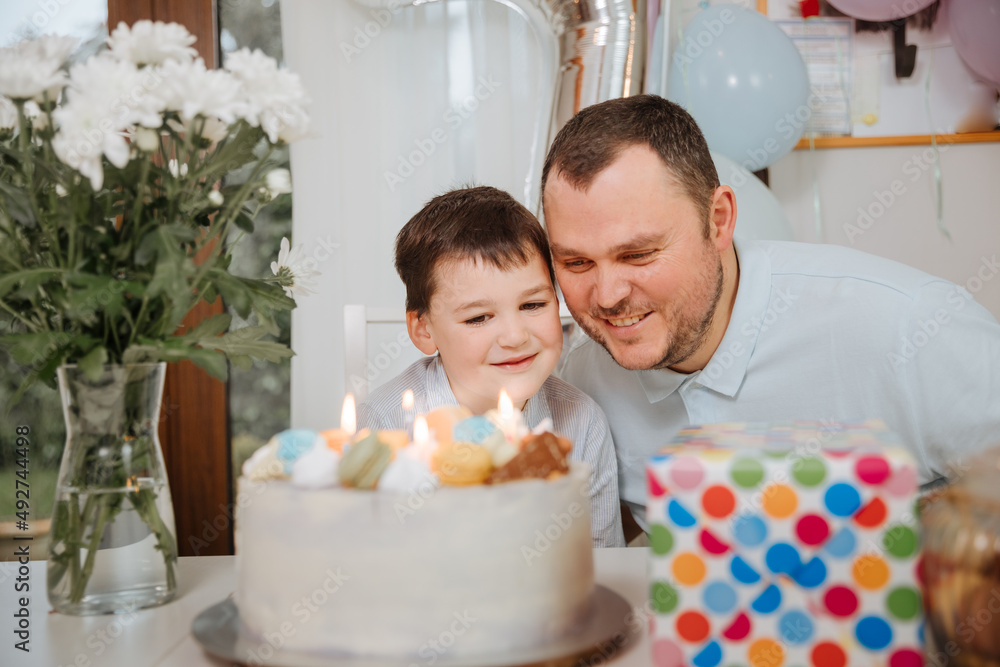 Father with son celebrate children's birthday party at home. Child is 7 years old and blows the candles on the cake. Single father with his son 