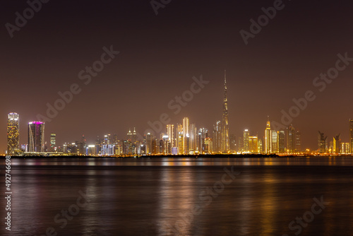 Dubai Business Bay skyline at night with colorful illuminated buildings and calm Dubai Creek water.