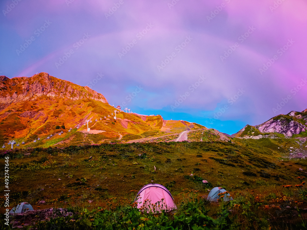 Tourist tents in the mountains of Krasnaya Polyana (Sochi) in summer. A rainbow in the sunset sky.