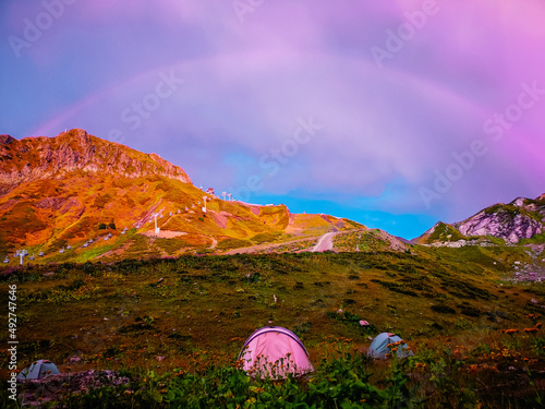 Obraz na płótnie Tourist tents in the mountains of Krasnaya Polyana (Sochi) in summer. A rainbow in the sunset sky. w salonie