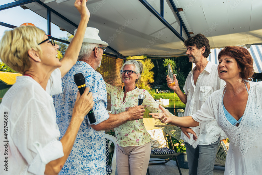 Senior people singing karaoke celebrating birthday in the cottage on the river.
