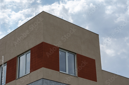 A beige and brown building against a cloudy sky. A rectangular structure with a straight roof.