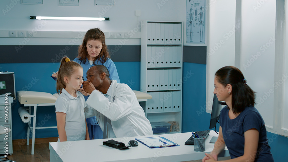 Physician using otoscope to do ear examination in cabinet, talking to nurse about diagnosis. Male doctor with otology instrument consulting child with infection. Otologist examining patient.